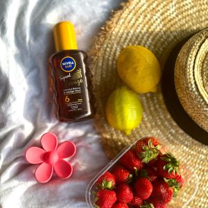 Flat lay of summer essentials: sunscreen, strawberries, lemons, and a straw hat on a blanket.