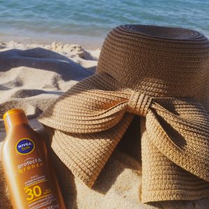 A sun hat and sunscreen on a sandy beach by the ocean, perfect for summer.